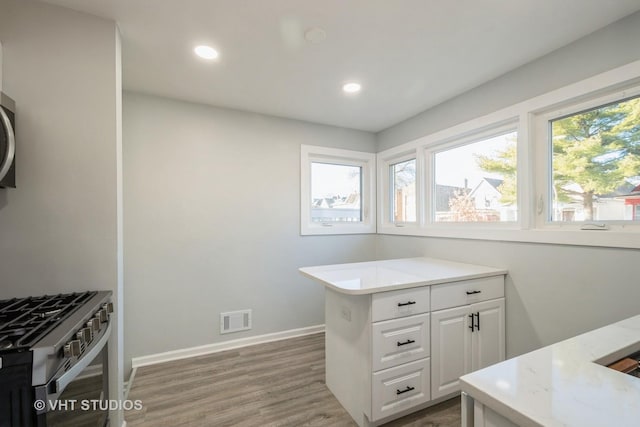 kitchen featuring visible vents, gas stove, white cabinets, wood finished floors, and baseboards