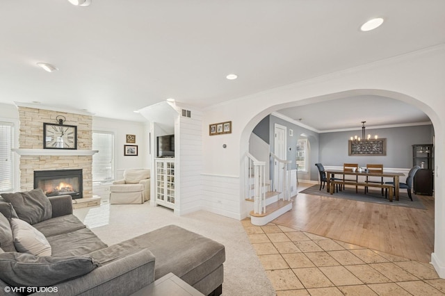 living room featuring light tile patterned flooring, a notable chandelier, a fireplace, ornamental molding, and stairway