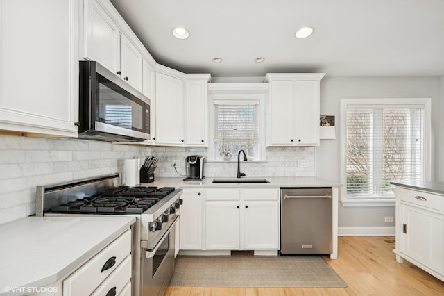 kitchen featuring appliances with stainless steel finishes, white cabinetry, a sink, and backsplash