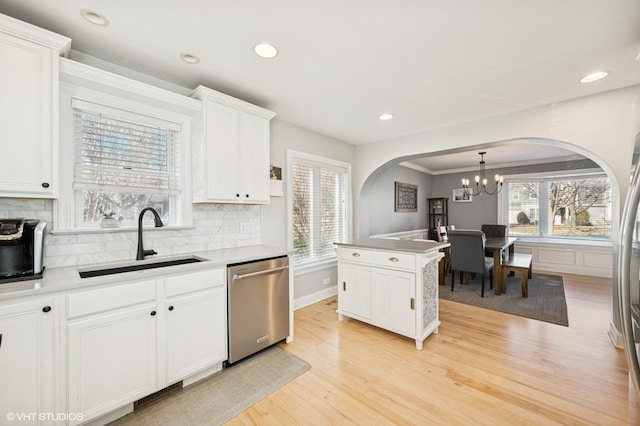 kitchen featuring tasteful backsplash, stainless steel dishwasher, white cabinets, a sink, and light wood-type flooring