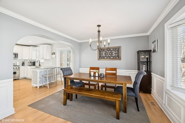 dining space featuring arched walkways, light wood-style flooring, visible vents, wainscoting, and crown molding