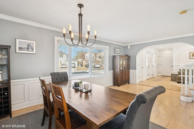 dining area featuring a wainscoted wall, light wood-style flooring, arched walkways, and ornamental molding