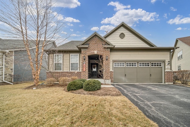 view of front of house with aphalt driveway, a front yard, brick siding, and a garage