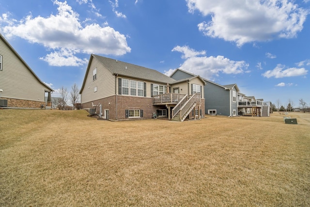 rear view of house featuring brick siding, a lawn, stairway, central AC, and a wooden deck