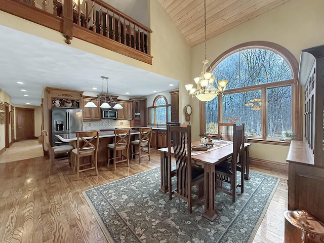 dining room with baseboards, high vaulted ceiling, light wood finished floors, and an inviting chandelier