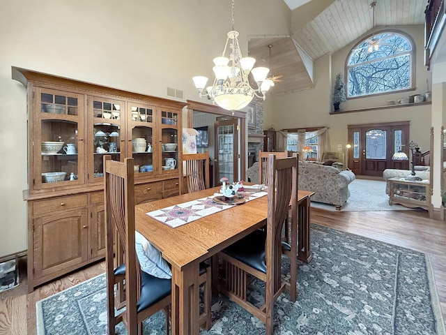 dining space with visible vents, an inviting chandelier, light wood-type flooring, a fireplace, and high vaulted ceiling