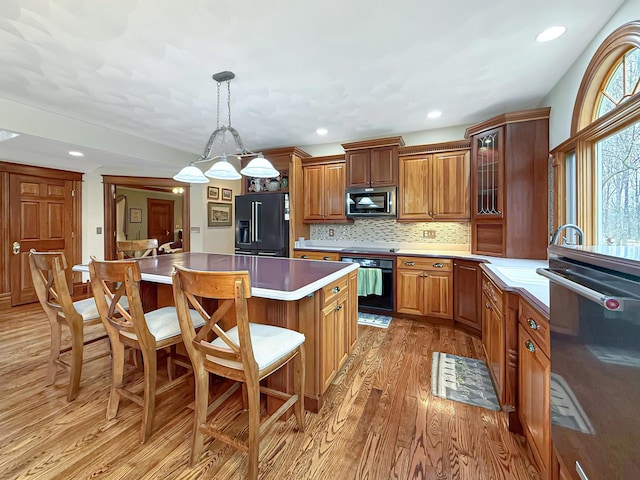 kitchen featuring a center island, brown cabinets, light wood-style flooring, high quality fridge, and a kitchen breakfast bar