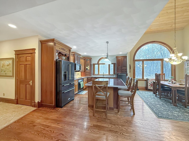 kitchen with pendant lighting, appliances with stainless steel finishes, a kitchen island, wood finished floors, and a kitchen breakfast bar