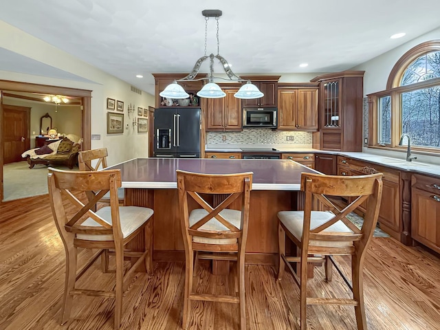 kitchen with tasteful backsplash, range, light wood-style flooring, glass insert cabinets, and high end black refrigerator