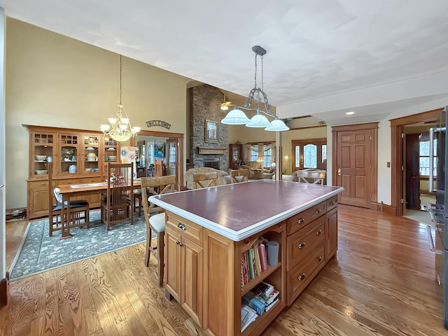 kitchen with a stone fireplace, light wood-style flooring, a center island, open shelves, and decorative light fixtures