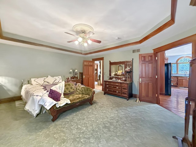 bedroom featuring a tray ceiling, freestanding refrigerator, visible vents, and baseboards