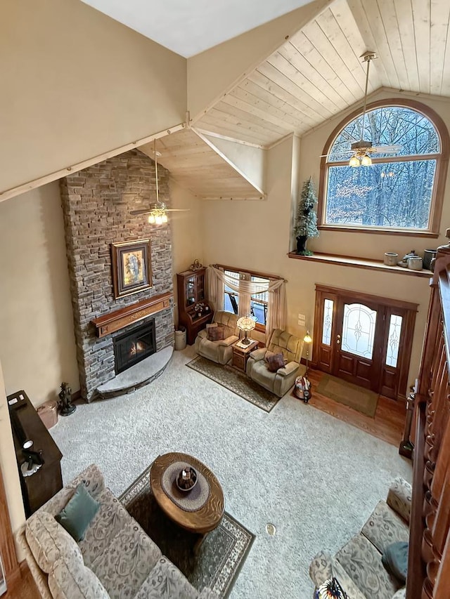 carpeted living area featuring wooden ceiling, high vaulted ceiling, and a stone fireplace