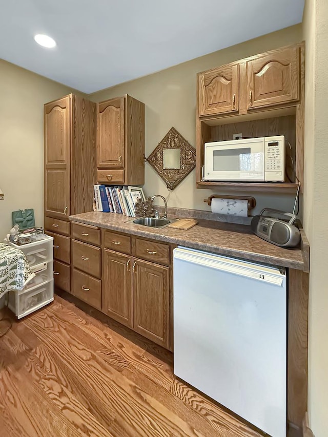 kitchen with white appliances, light wood-style flooring, and a sink