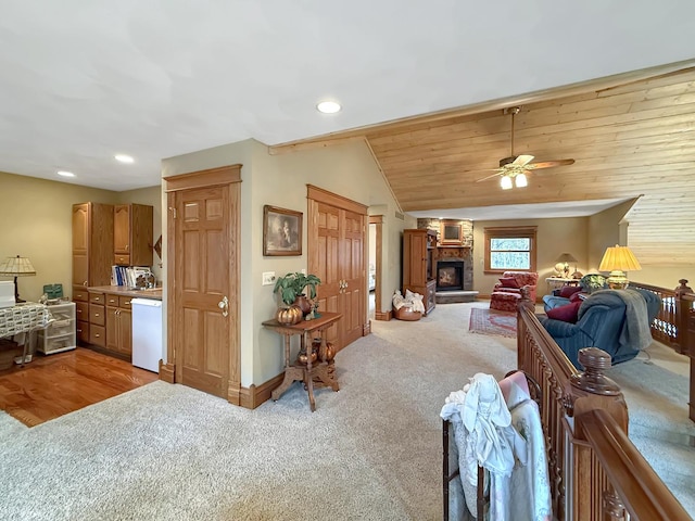 carpeted living area featuring vaulted ceiling, a stone fireplace, baseboards, and recessed lighting