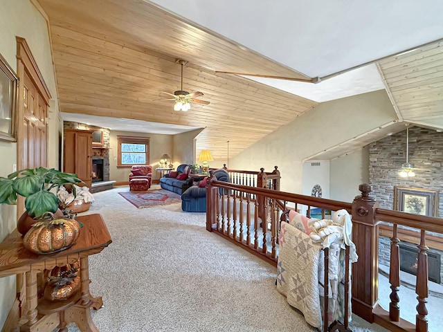 living room featuring lofted ceiling, ceiling fan, a stone fireplace, wooden ceiling, and carpet flooring