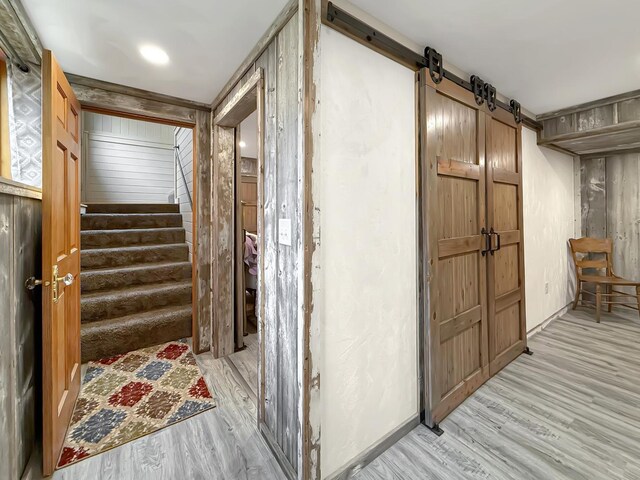 corridor with stairs, a barn door, light wood-style flooring, and baseboards