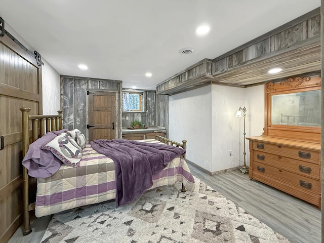 bedroom with recessed lighting, visible vents, a barn door, light wood-style floors, and baseboards