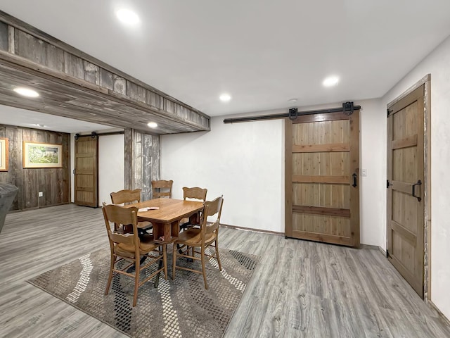 dining room featuring light wood-style floors, a barn door, wooden walls, and recessed lighting