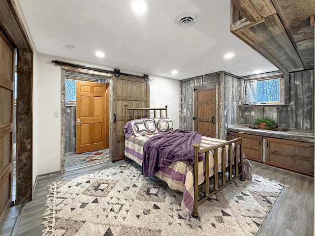 bedroom featuring a barn door, light wood-type flooring, visible vents, and recessed lighting