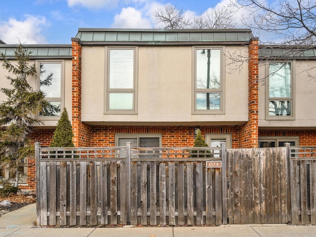 view of side of home featuring brick siding, a fenced front yard, and stucco siding