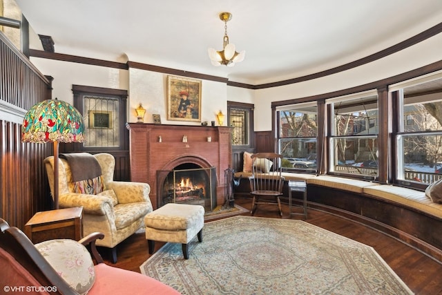 sitting room with an inviting chandelier, ornamental molding, a brick fireplace, wainscoting, and wood finished floors