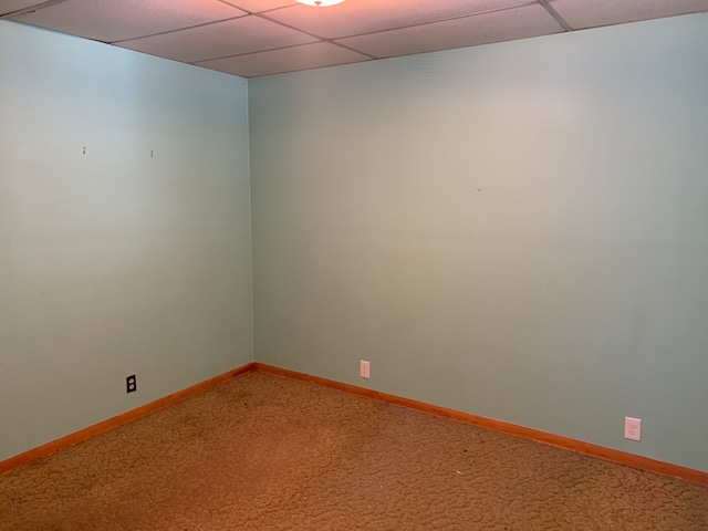 empty room featuring a paneled ceiling, carpet, and baseboards