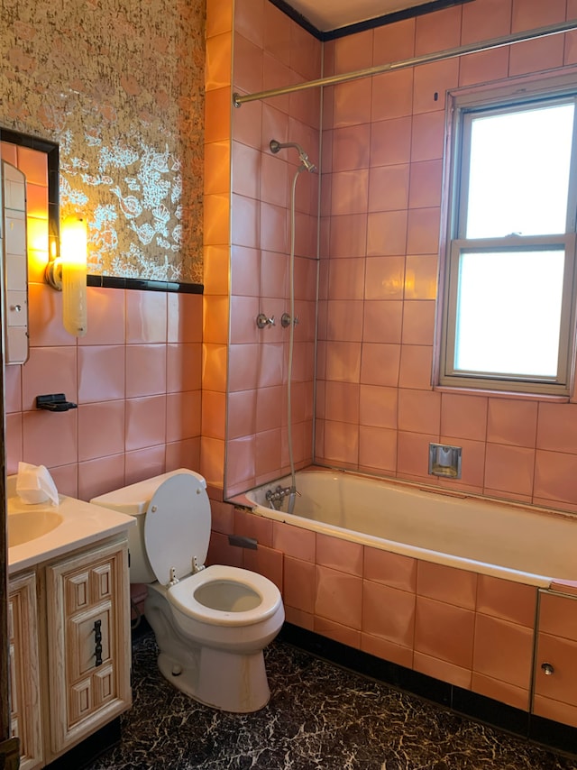 full bath featuring toilet, a wainscoted wall, tiled shower / bath combo, vanity, and tile walls