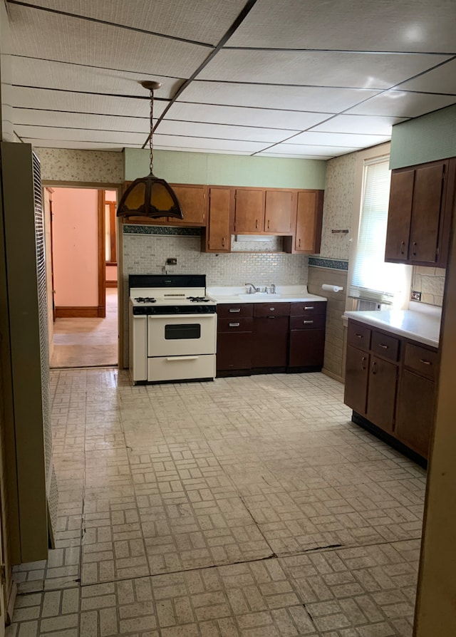 kitchen with white gas range oven, decorative light fixtures, a sink, light countertops, and brick patterned floor