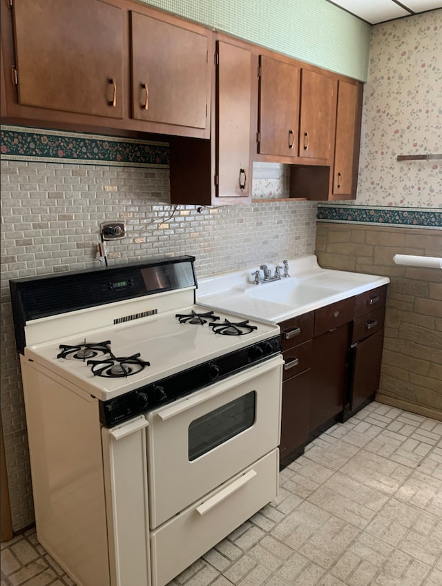 kitchen with wallpapered walls, white range with gas stovetop, a wainscoted wall, light countertops, and a sink