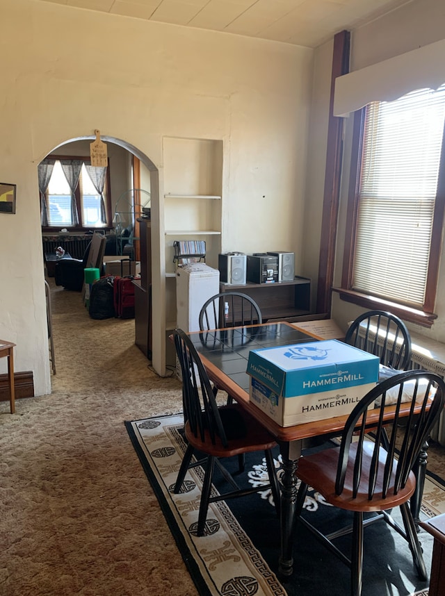 dining room featuring a wealth of natural light, arched walkways, and carpet flooring