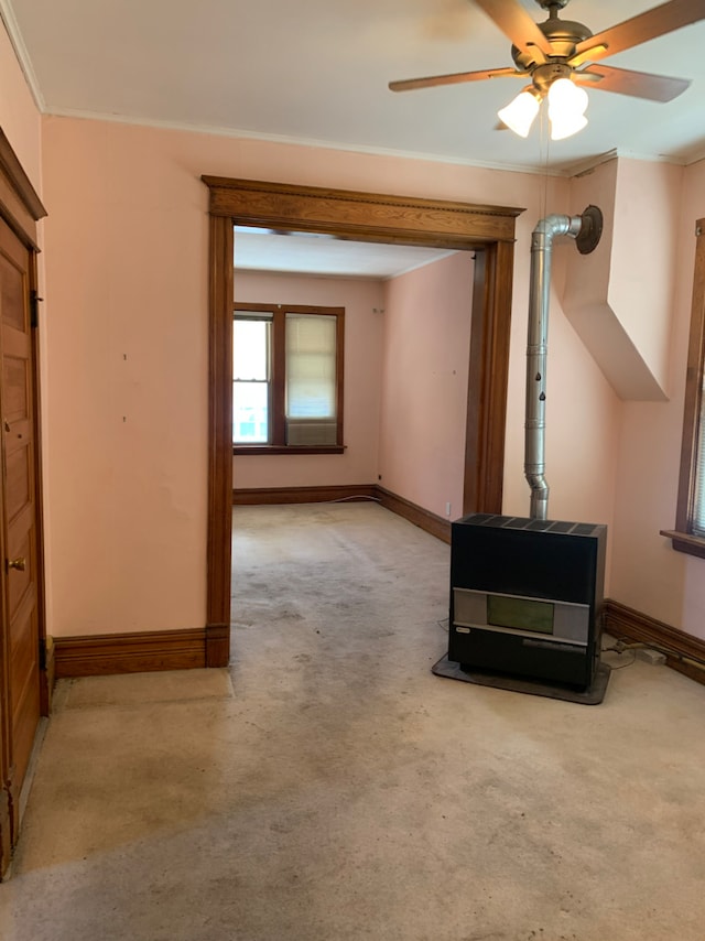 unfurnished living room featuring a wood stove, baseboards, ornamental molding, and light colored carpet