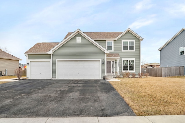 traditional home featuring aphalt driveway, a garage, a shingled roof, fence, and a front lawn