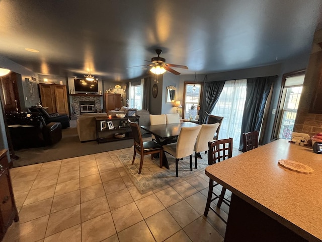 dining area with a healthy amount of sunlight, tile patterned flooring, a ceiling fan, and a glass covered fireplace