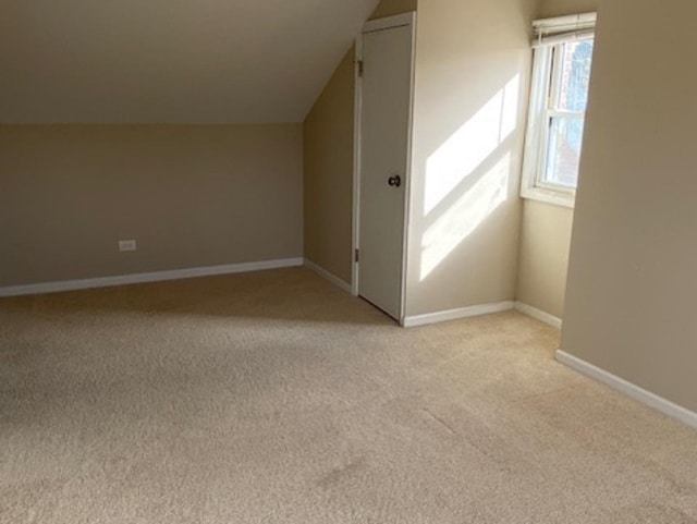 additional living space featuring baseboards, vaulted ceiling, and light colored carpet