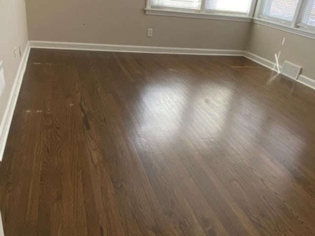 empty room with dark wood-style floors, visible vents, a wealth of natural light, and baseboards