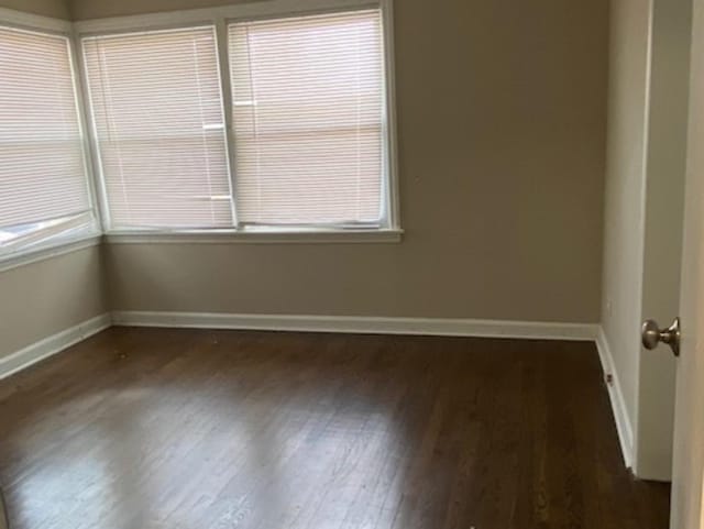 spare room with dark wood finished floors, plenty of natural light, and baseboards