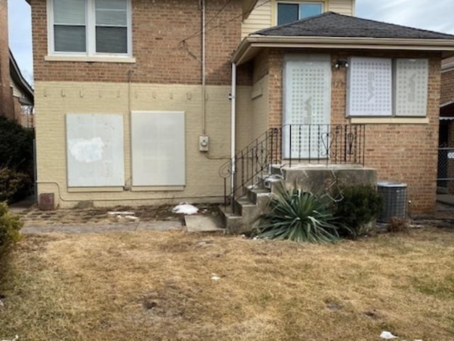 back of house featuring brick siding, a lawn, and central AC