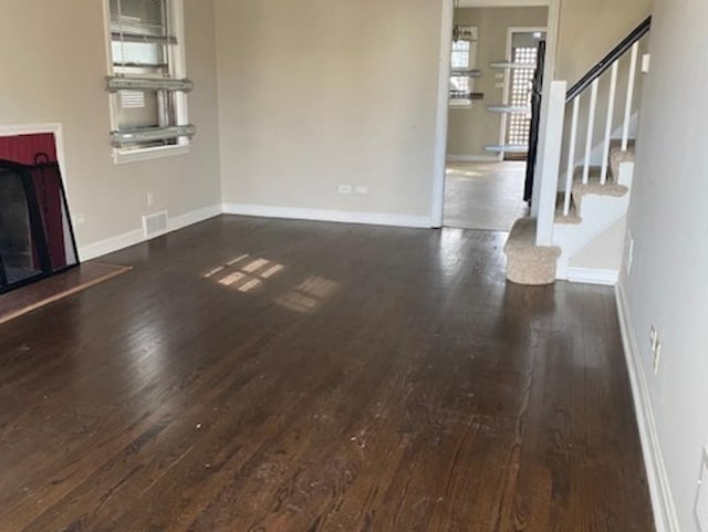 unfurnished living room featuring dark wood-style flooring, a fireplace with raised hearth, stairway, and baseboards