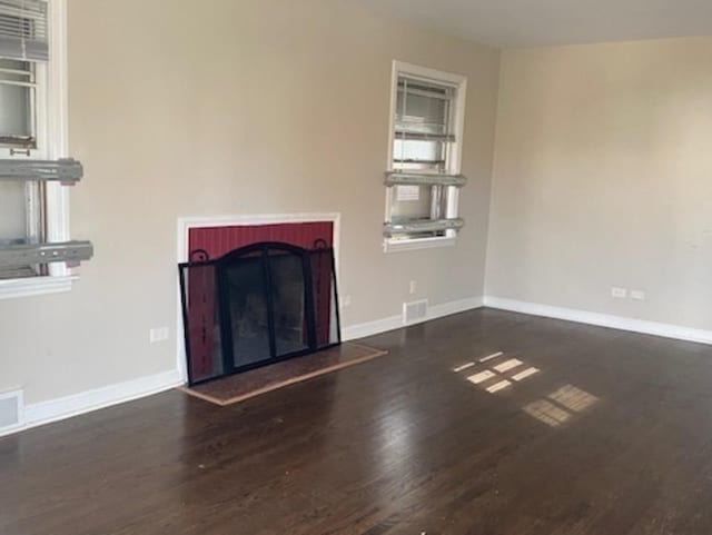 unfurnished living room featuring a fireplace with raised hearth, dark wood-type flooring, visible vents, and baseboards