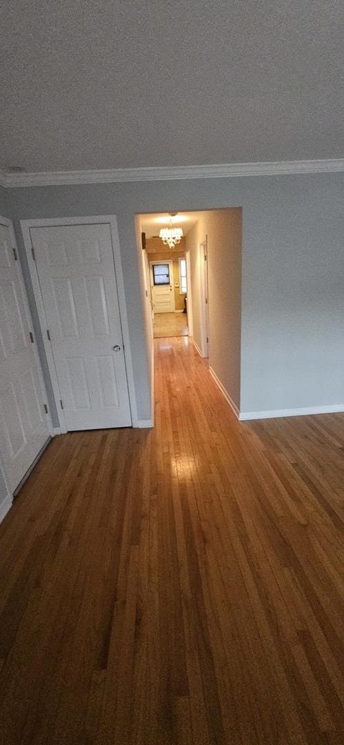 hallway with crown molding, baseboards, a notable chandelier, and wood finished floors