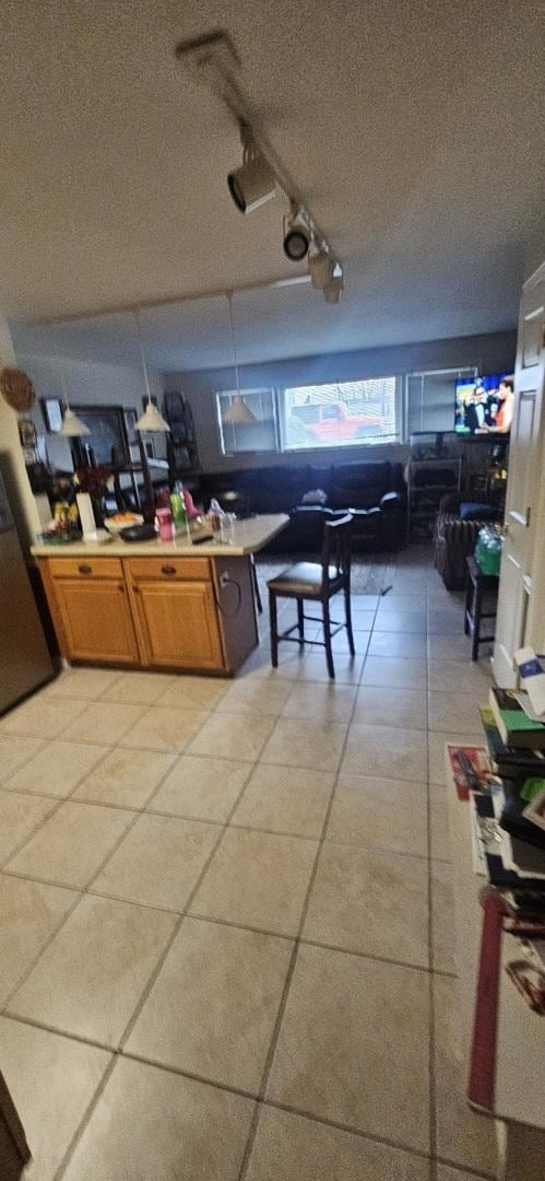 kitchen featuring brown cabinets, light countertops, freestanding refrigerator, light tile patterned flooring, and a textured ceiling