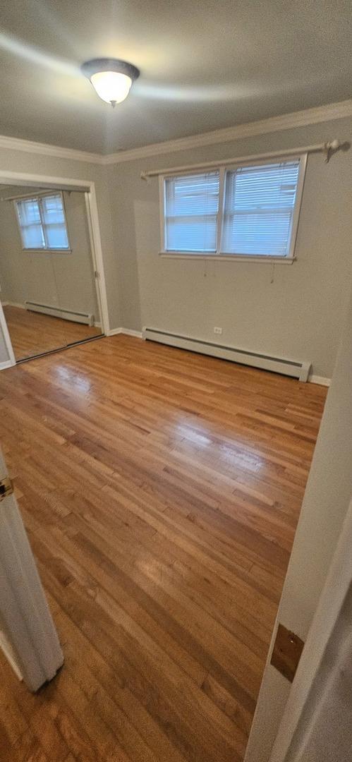 empty room with a baseboard radiator, a wealth of natural light, baseboard heating, ornamental molding, and wood finished floors