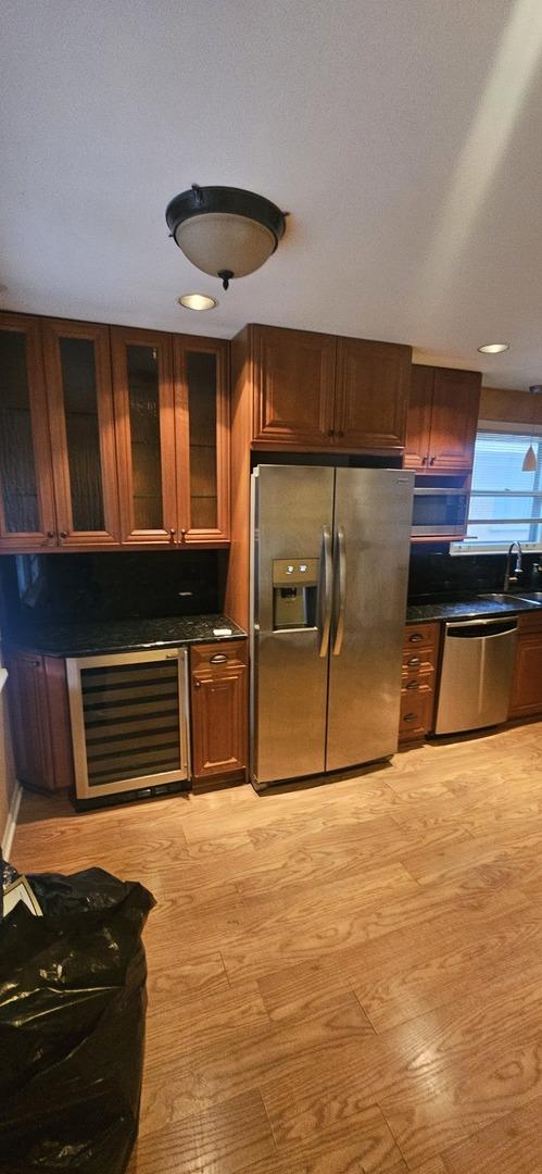 kitchen with dark countertops, wine cooler, glass insert cabinets, stainless steel appliances, and a sink