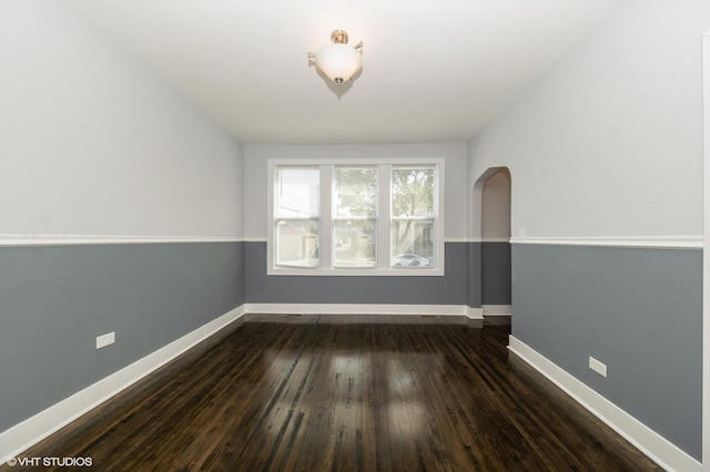 unfurnished room featuring arched walkways, dark wood-type flooring, and baseboards