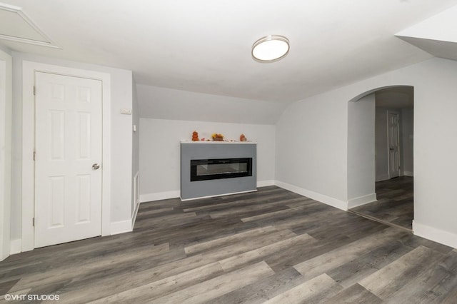 unfurnished living room featuring dark wood-style floors, arched walkways, lofted ceiling, a glass covered fireplace, and baseboards