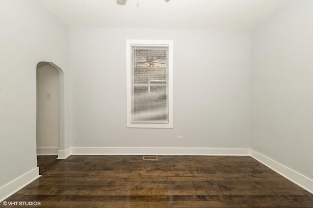 empty room featuring dark wood-style floors, arched walkways, visible vents, and baseboards