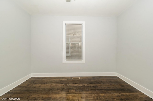 empty room featuring dark wood-style flooring, visible vents, and baseboards