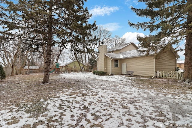 snow covered rear of property featuring fence and a chimney