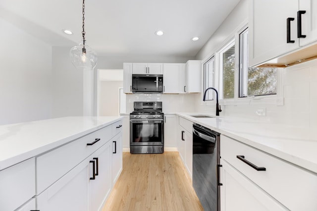 kitchen with black dishwasher, hanging light fixtures, white cabinetry, a sink, and stainless steel gas range oven