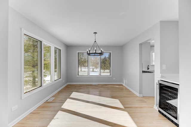 unfurnished dining area with light wood finished floors, beverage cooler, visible vents, baseboards, and a notable chandelier